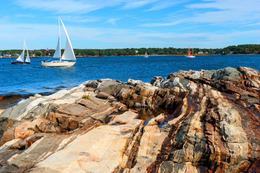 A rugged rocky shoreline with waves gently crashing against the stones under a clear blue sky