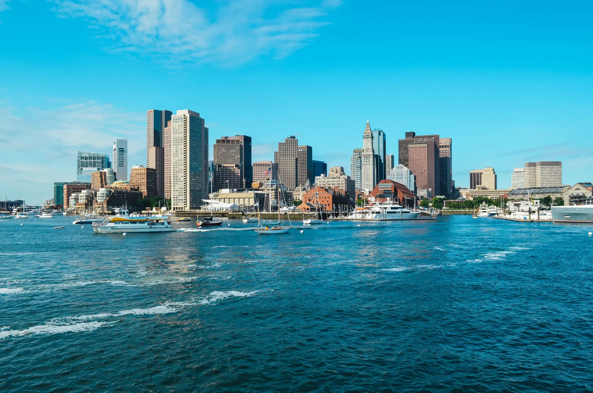 City skyline viewed from the harbor, showcasing tall buildings against a clear blue sky and calm water